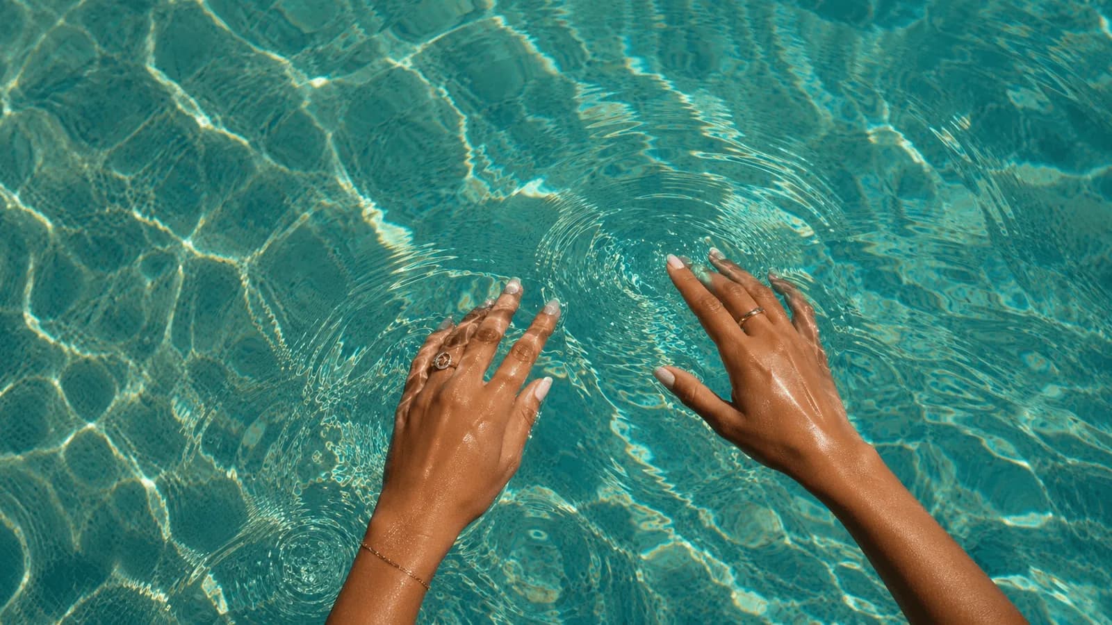 Mains qui effleurent une eau de piscine très claire.