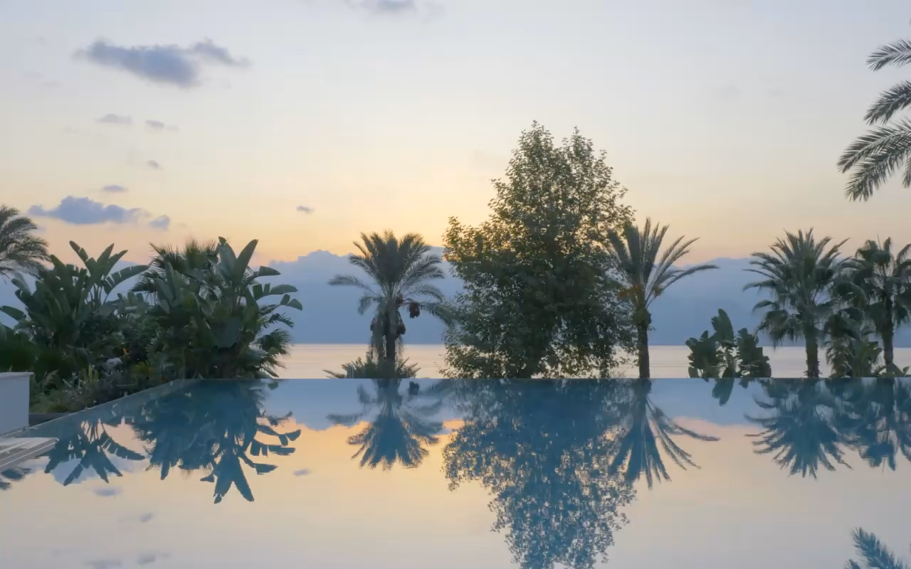 Piscine à débordement au soleil couchant, puis le bassin d'une villa bordé de transats.