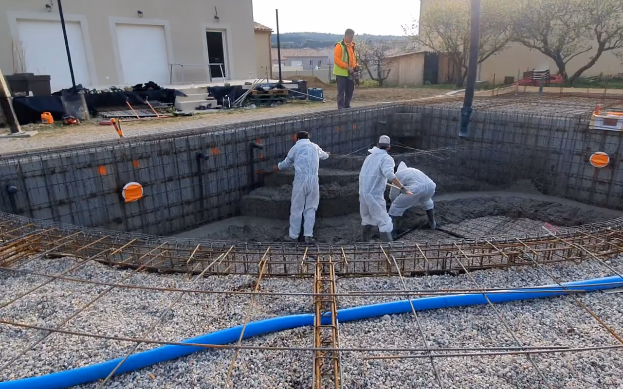 Le fond d'un bassin ferraillé sur son hérisson de gravier, juste avant le coulage, la pompe à béton au-dessus.
