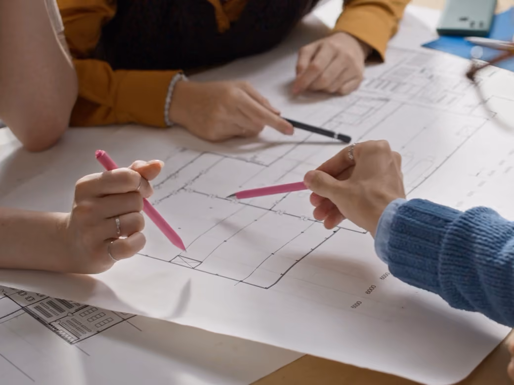 Des mains et des crayons sur un plan de niveau : on discute le projet sur plan.