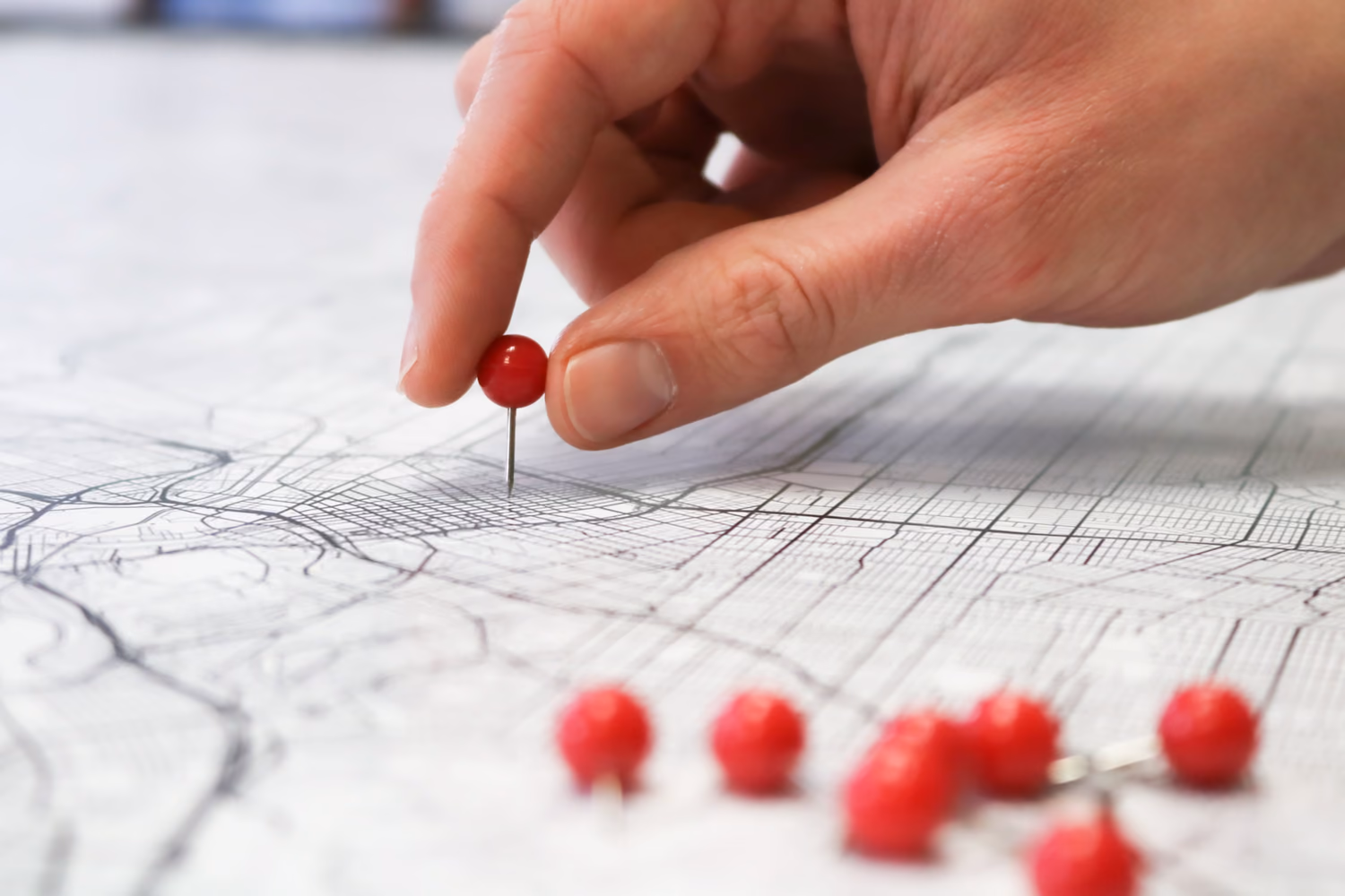 Une main plante une épingle rouge sur une carte : la zone où chercher le terrain.