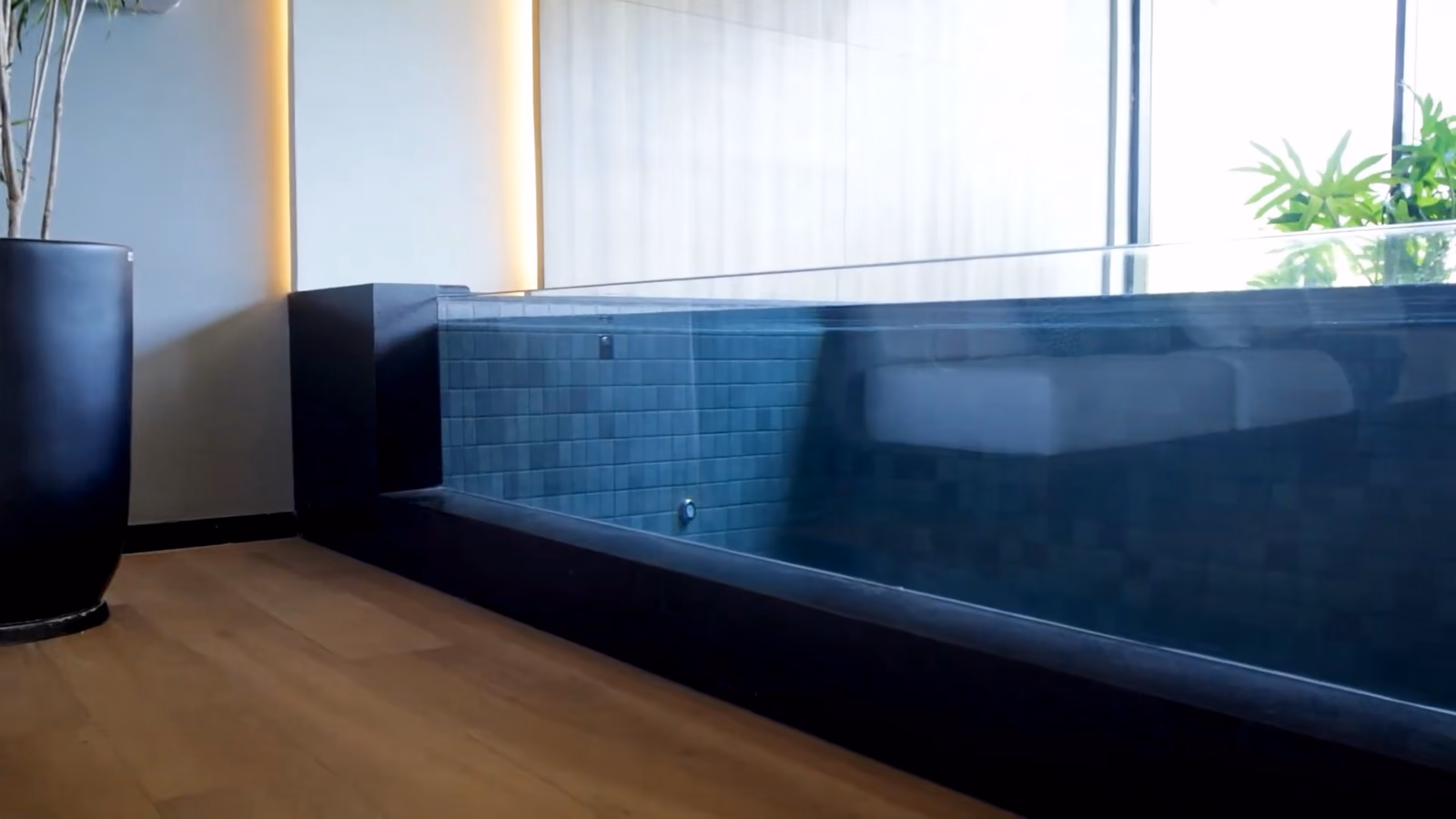 Bassin intérieur au carrelage bleu sombre, paroi transparente, devant de grandes baies vitrées.