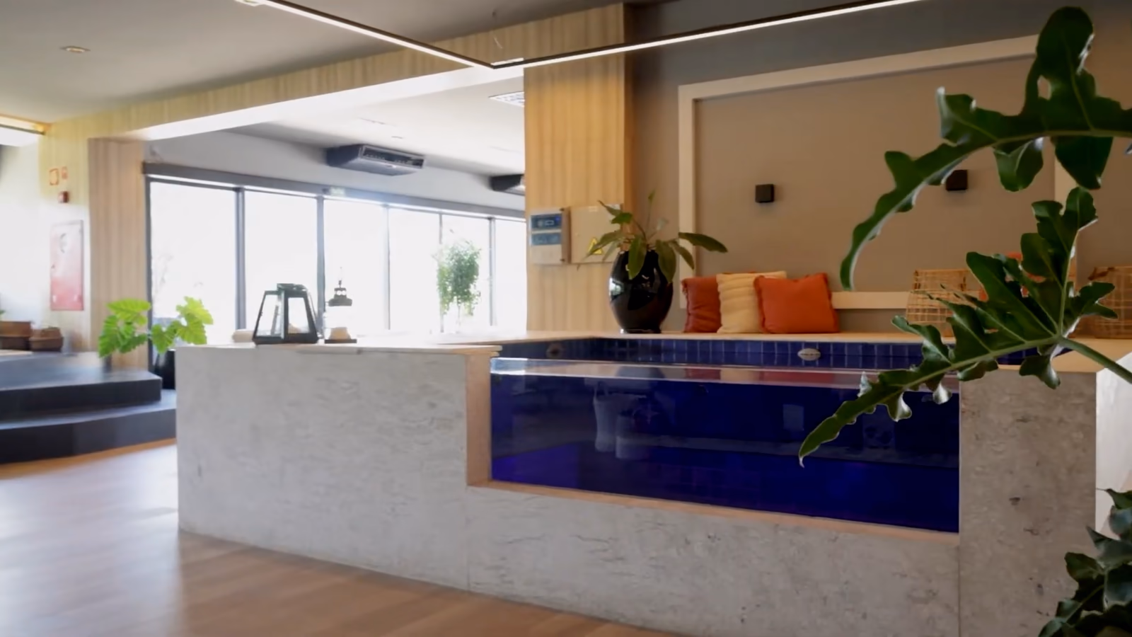 Salon lumineux : un bassin à paroi transparente encastré dans un comptoir en pierre, eau bleu nuit.