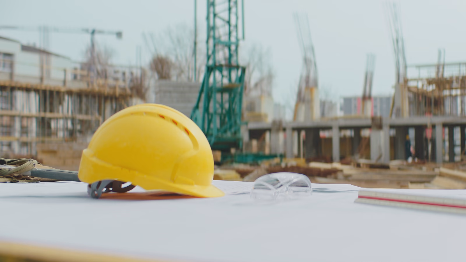 Casque de chantier jaune posé sur des plans, chantier d'immeuble flou derrière.