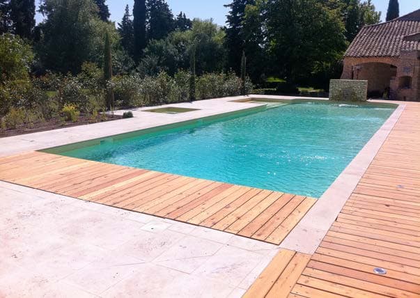 Piscine rectangulaire bordée d'une plage en lames de bois, mas en pierre.