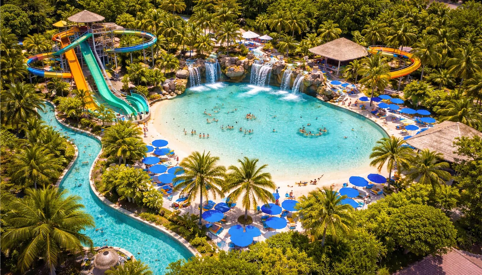Parc aquatique vu du ciel : bassin à plage, cascades, rivière lente, tours de toboggans.