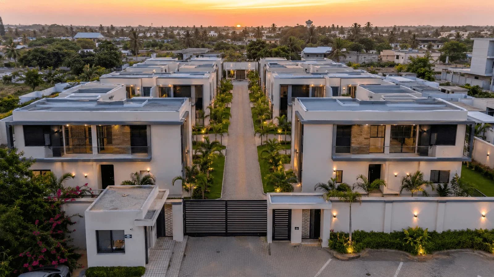 Résidence de villas jumelées à étage de part et d'autre d'une allée, vue du ciel au crépuscule.