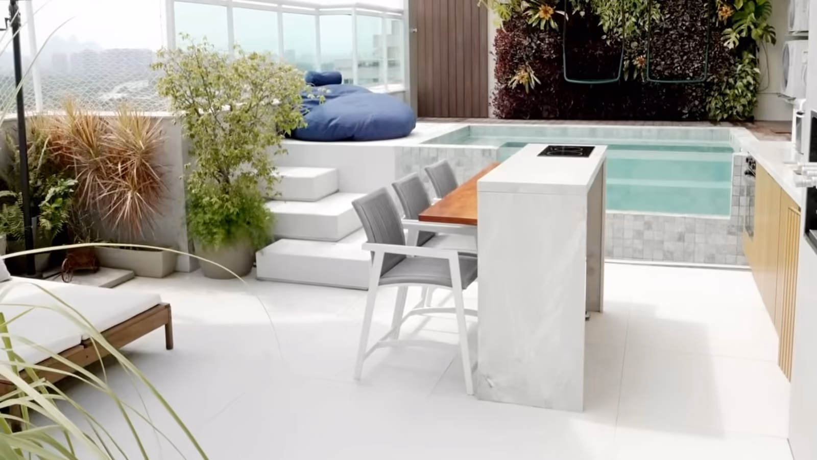 Toit-terrasse aménagé : un bassin derrière un bar en pierre claire, des plantes et un mur végétal.