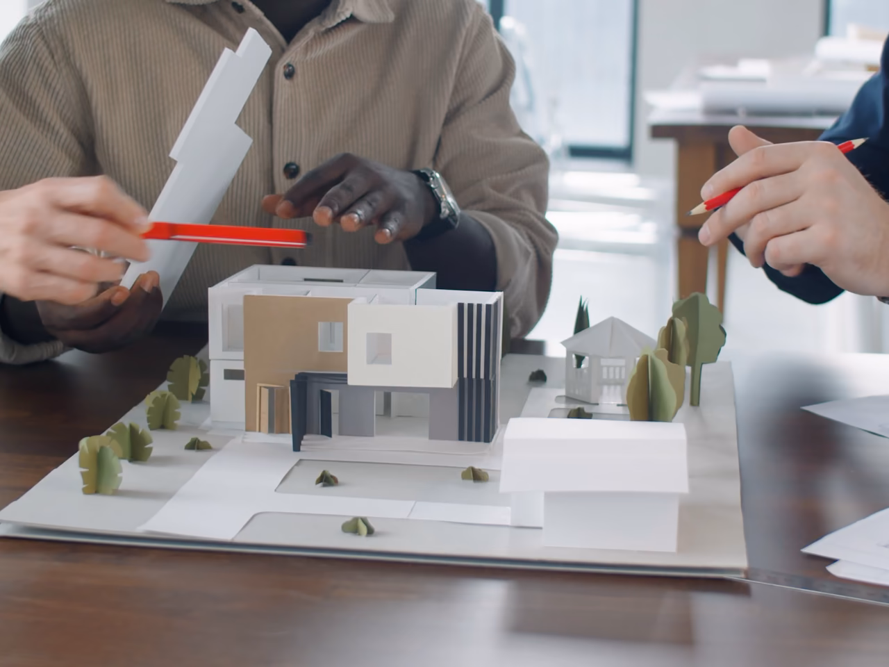 Pendant une réunion de conception, un crayon rouge désigne la maquette d'une villa à étage.