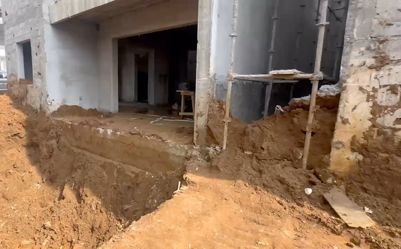 Chantier TIG : une fouille ouverte au pied d'un bâtiment en gros œuvre, puis une seconde fouille terrassée au soleil.