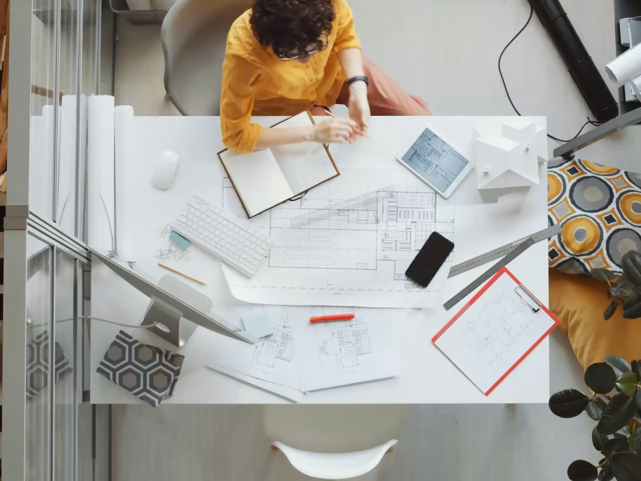 Vu du dessus, un rendez-vous autour de plans : poignée de main au-dessus de la table, puis échange en pointant le plan.