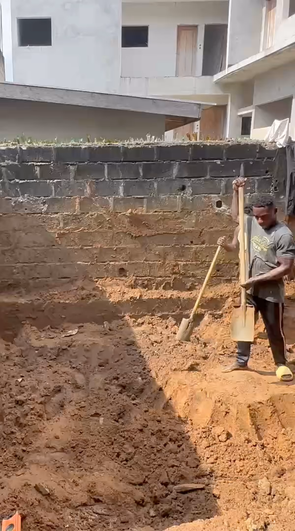 Filmé au téléphone sur notre chantier d'Abidjan : un ouvrier creuse à la pioche le fond d'une fouille de piscine, puis la fouille à redans contre le mur de clôture.