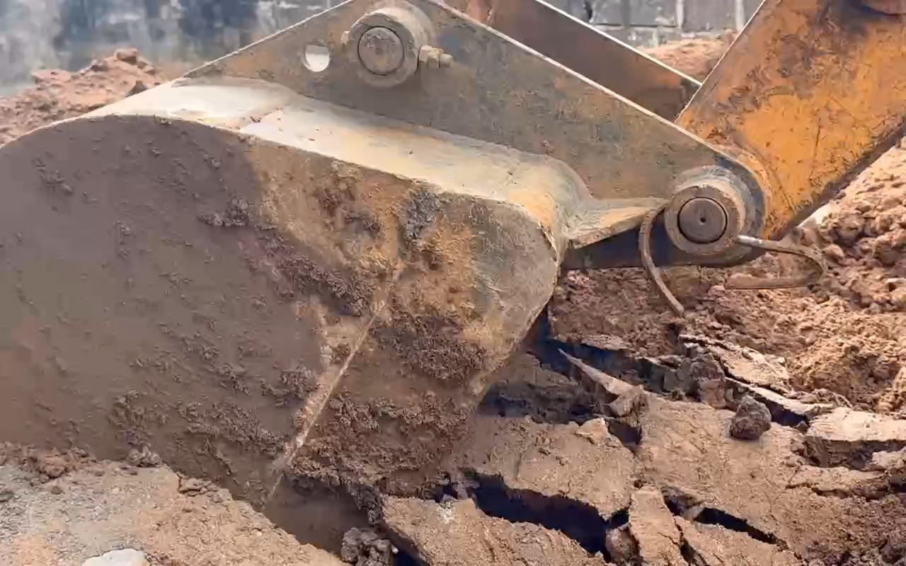Terrassement d'une piscine à Abidjan : le godet du tractopelle racle et pousse la terre, puis remblaie au pied du mur.