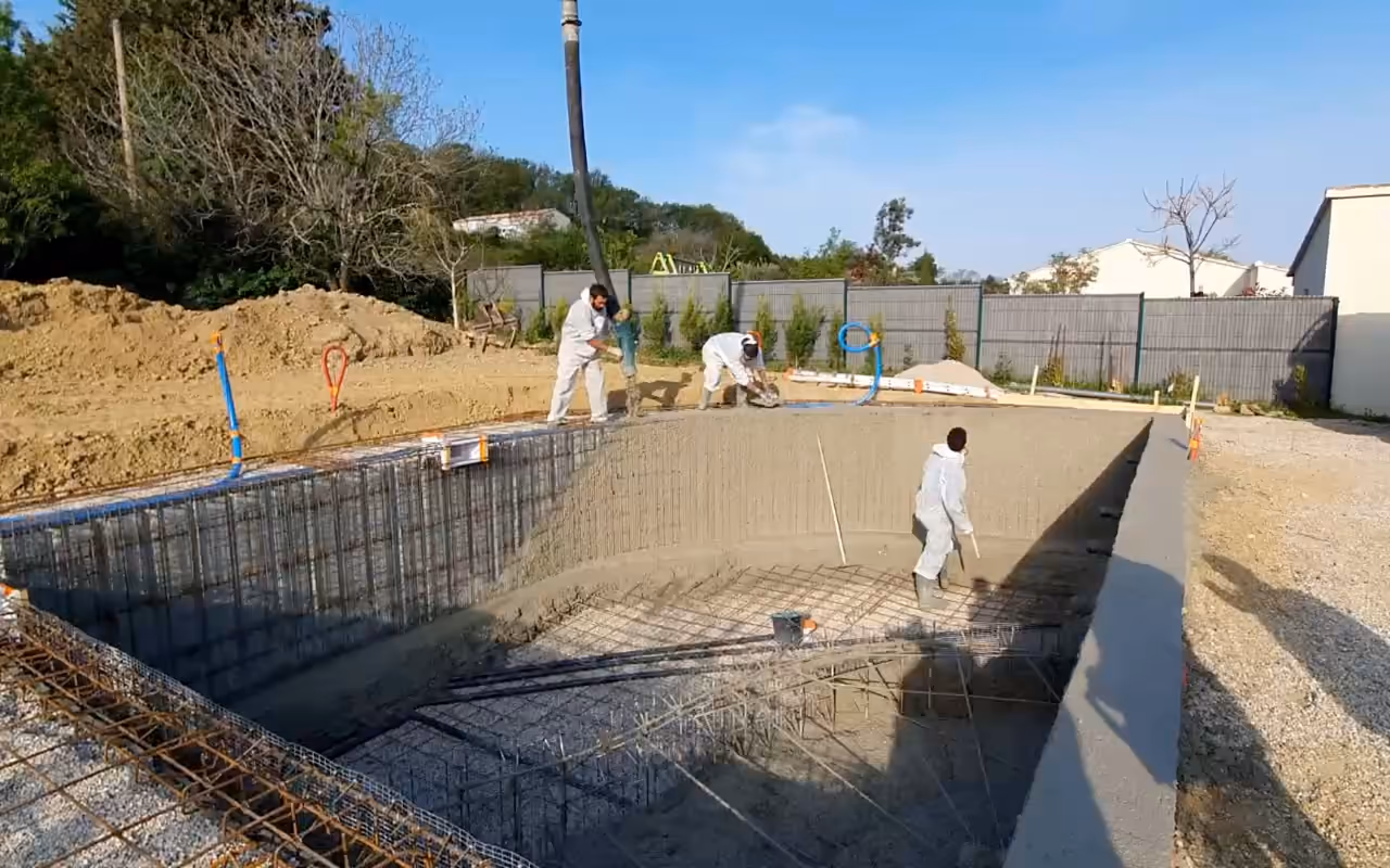 Piscine monobloc de forme libre en France : le grand bain aux voiles tout juste coulés, puis le bassin, ses marches romaines et sa plage fraîchement coulée.