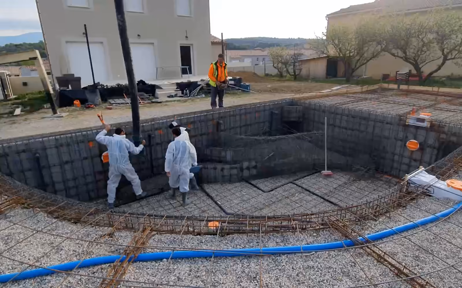 Coulage d'une piscine monobloc de forme libre en France : béton coulé dans les voiles en treillis, voile taloché, marches romaines en béton frais.