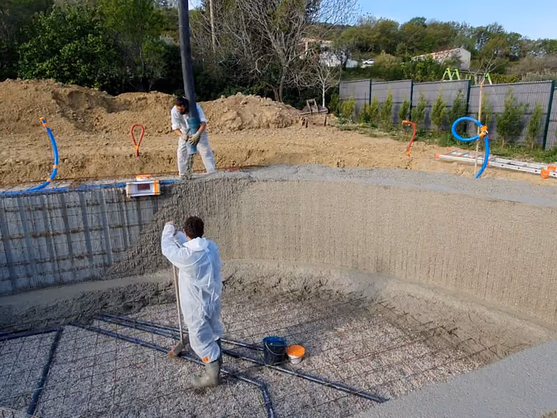 Un compagnon taloche le voile courbe en béton frais, au fond du bassin.