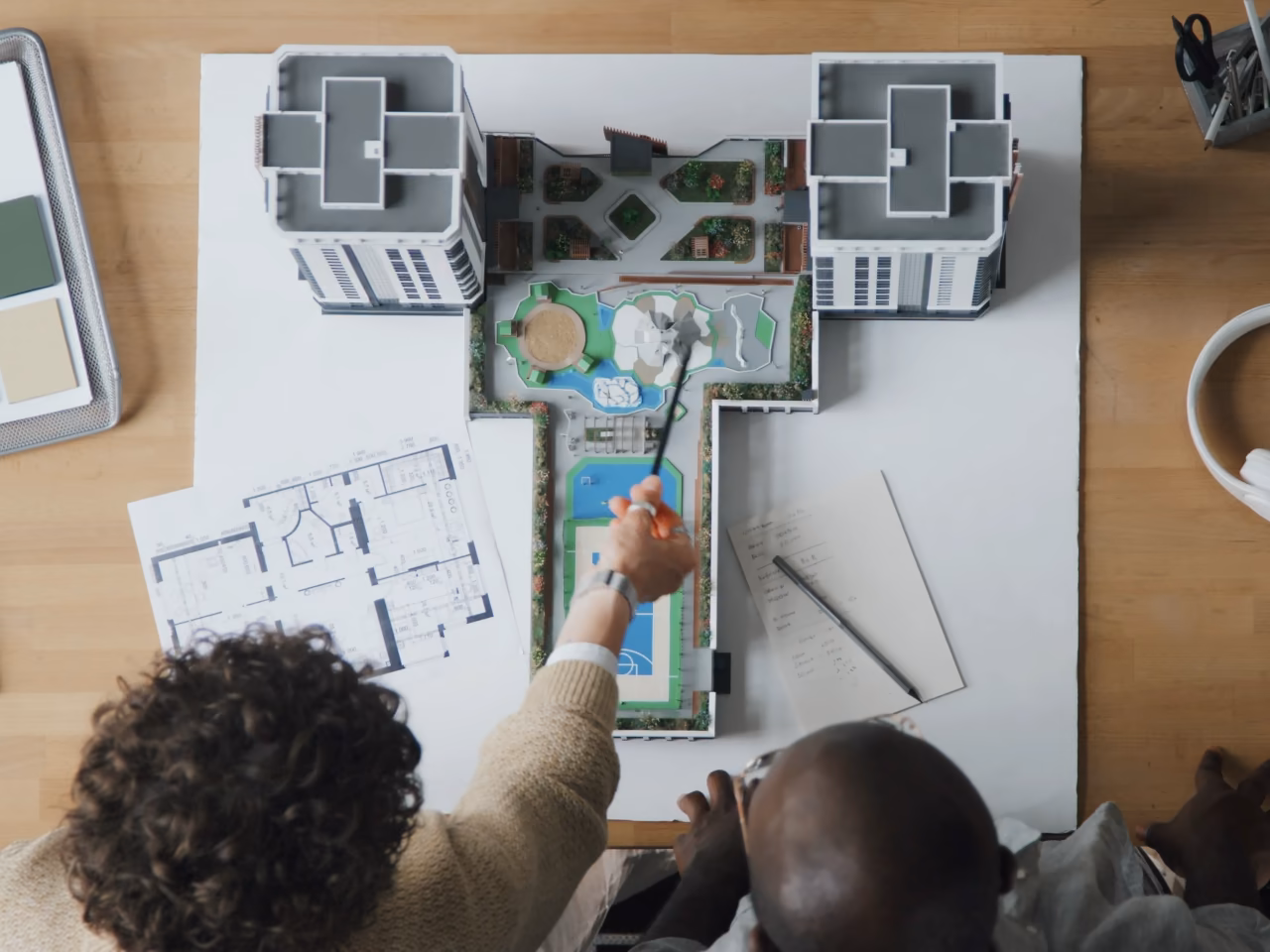 Vue du dessus : un crayon parcourt la maquette d'une résidence avec piscine, à côté des plans et d'un nuancier de matériaux.