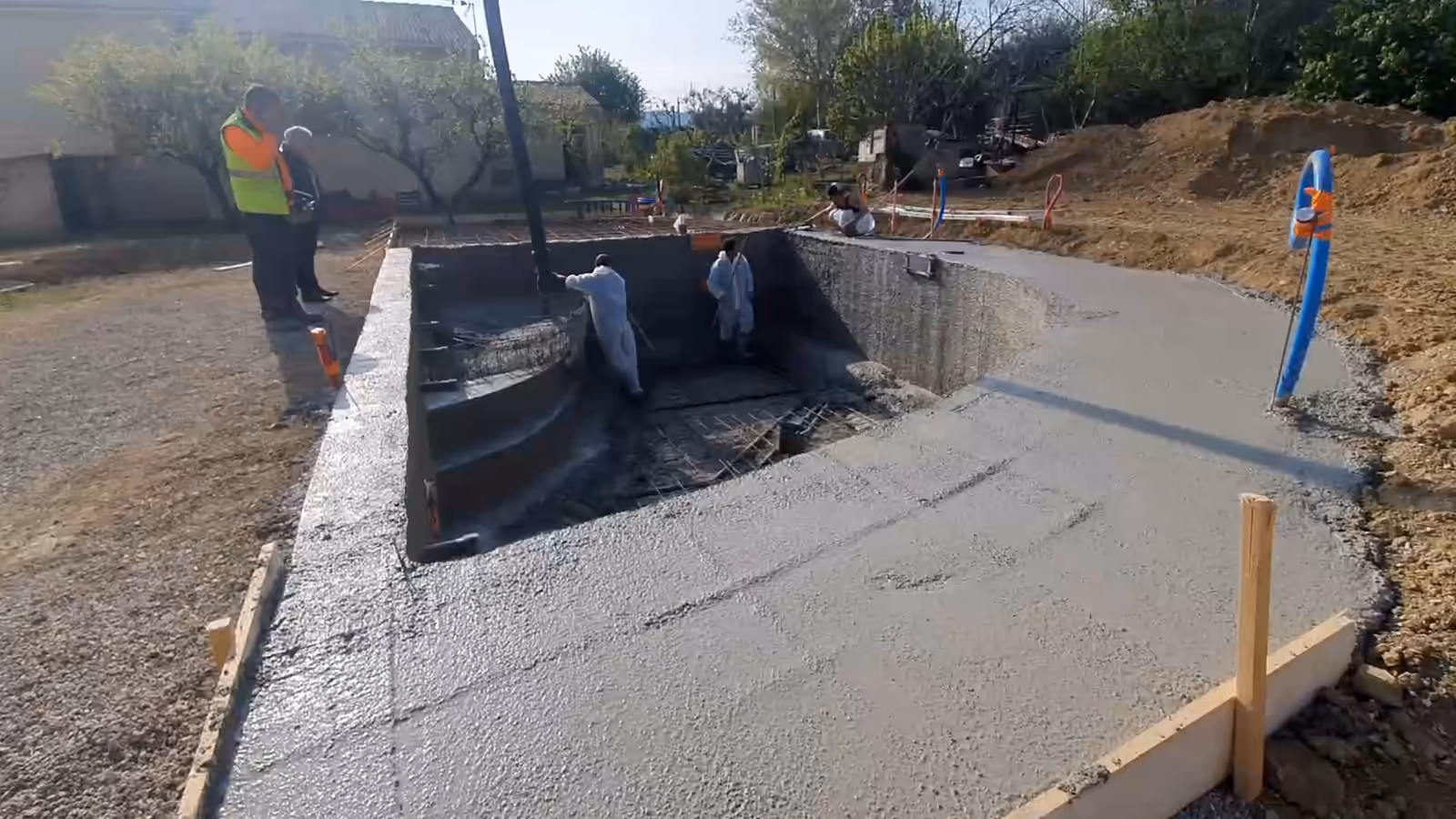 Chantier d'une piscine monobloc en France : la plage en béton frais coulée autour du bassin, puis la flèche de la pompe à béton au-dessus du voile courbe.