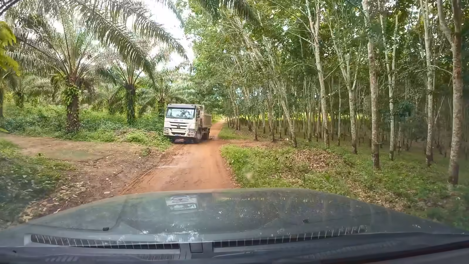 Une pelle ouvre un passage boueux dans la brousse, un camion déverse des rochers, une chargeuse pousse la latérite, puis la piste terminée vue du drone.
