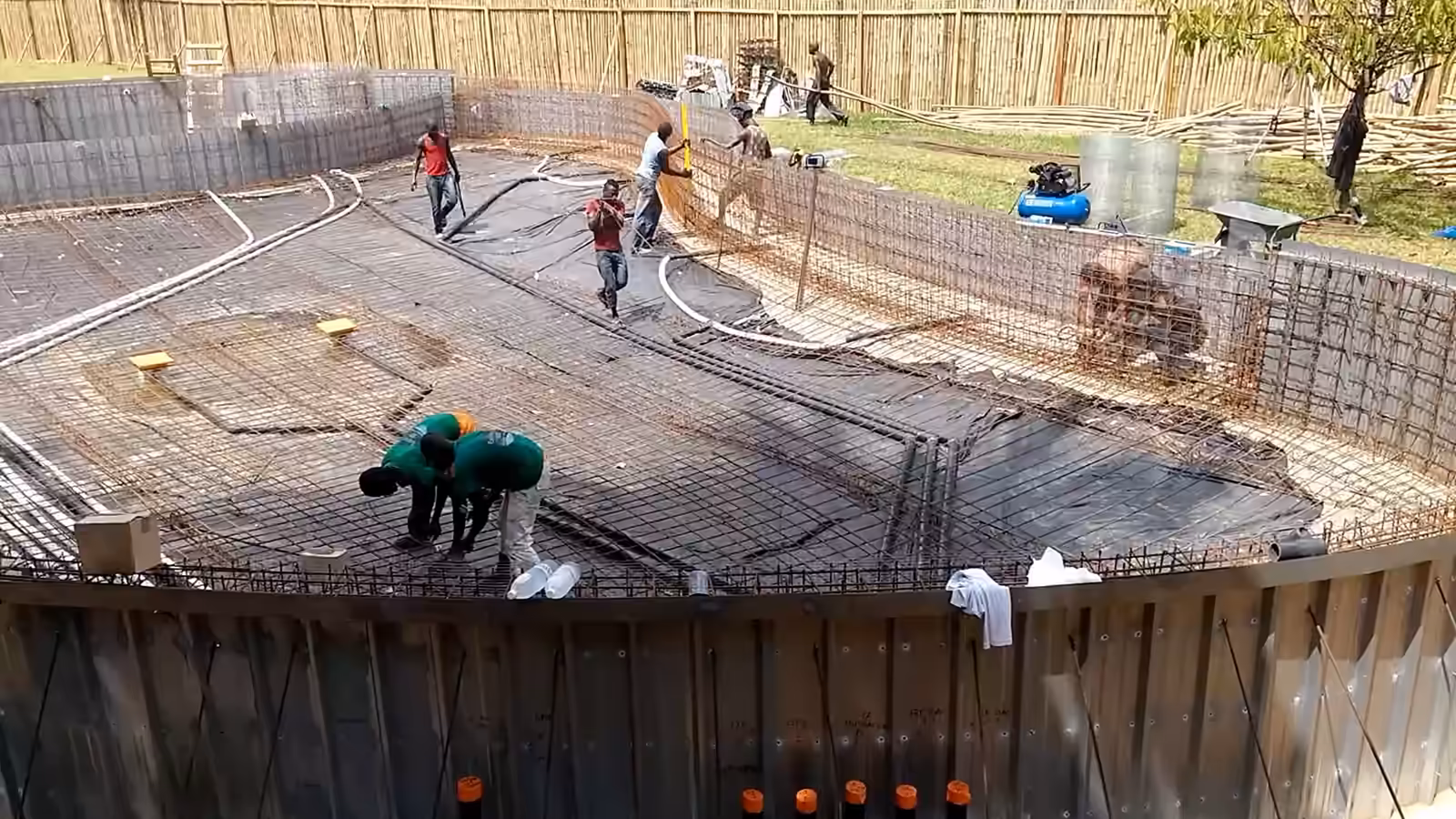 Chantier d'une piscine de forme libre : radier ferraillé, coulage du béton à la pompe, équipe qui tire le béton au râteau.
