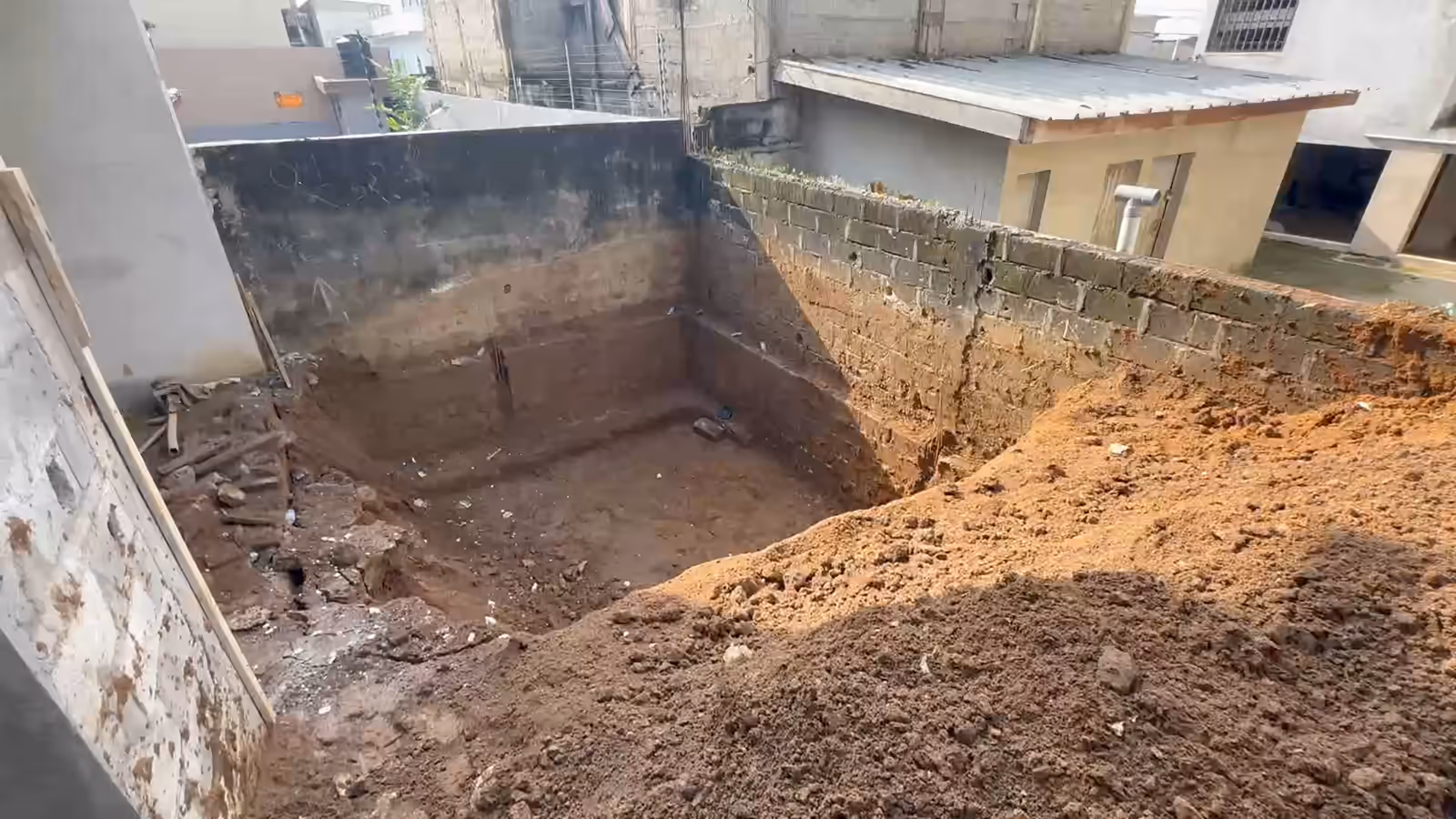 Les deux fouilles de piscine creusées à Abidjan : la première à redans contre le mur de clôture, le godet chargé du tractopelle, puis la seconde fouille en terre rouge au soleil.