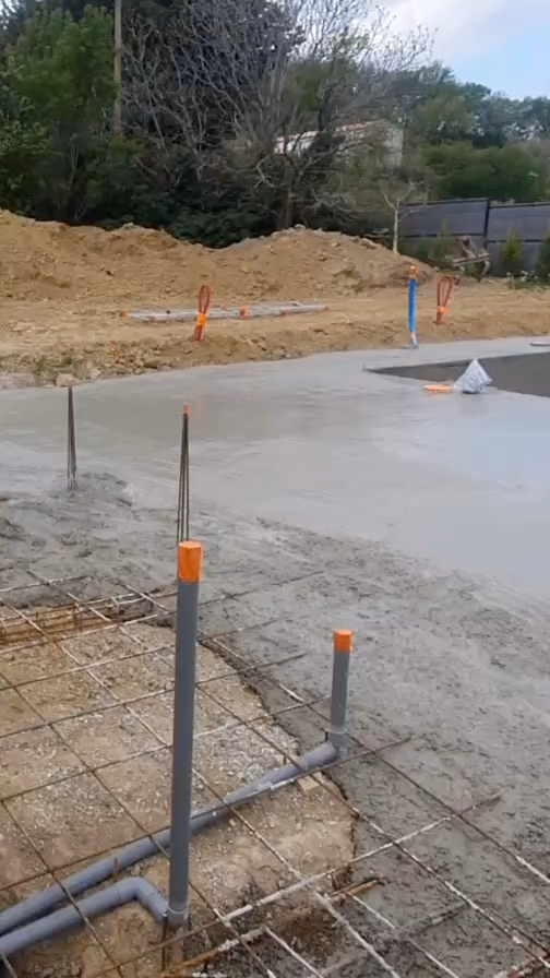 Des tuyaux d'évacuation en PVC gris posés dans le ferraillage, avec leurs attentes verticales bouchées en orange, pendant le coulage de la dalle.