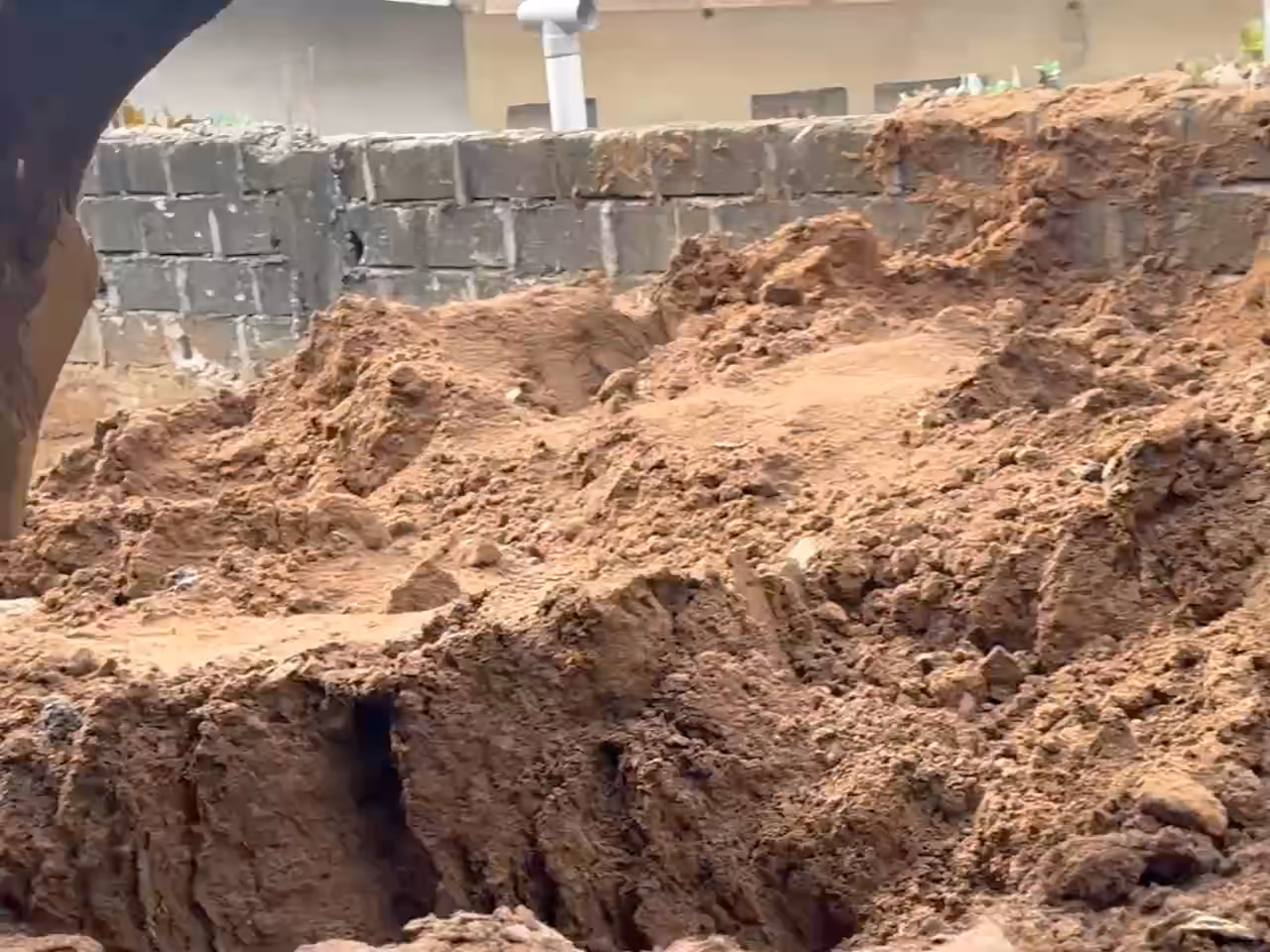 Le godet d'un tractopelle mord la terre et pousse les mottes, puis la fouille terminée, aux parois dressées en redans, sur un chantier de Trans Ivoire Groupe.
