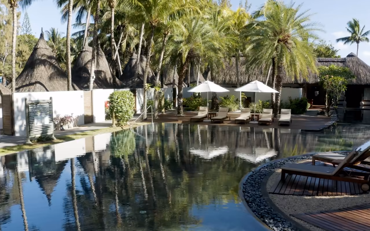 Bassin d'hôtel à fond sombre : les cocotiers, les parasols blancs et le ciel s'y reflètent comme dans un miroir.