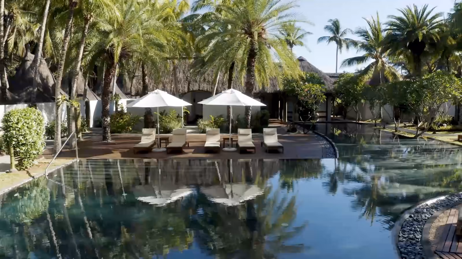 Grande piscine d'hôtel sous les cocotiers, transats et parasols, puis le chantier d'un grand bassin en mosaïque vu du ciel.