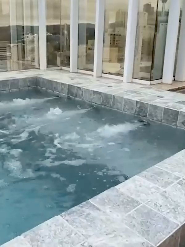 Eau en mouvement dans un bassin sur un toit-terrasse fermé de garde-corps vitrés.