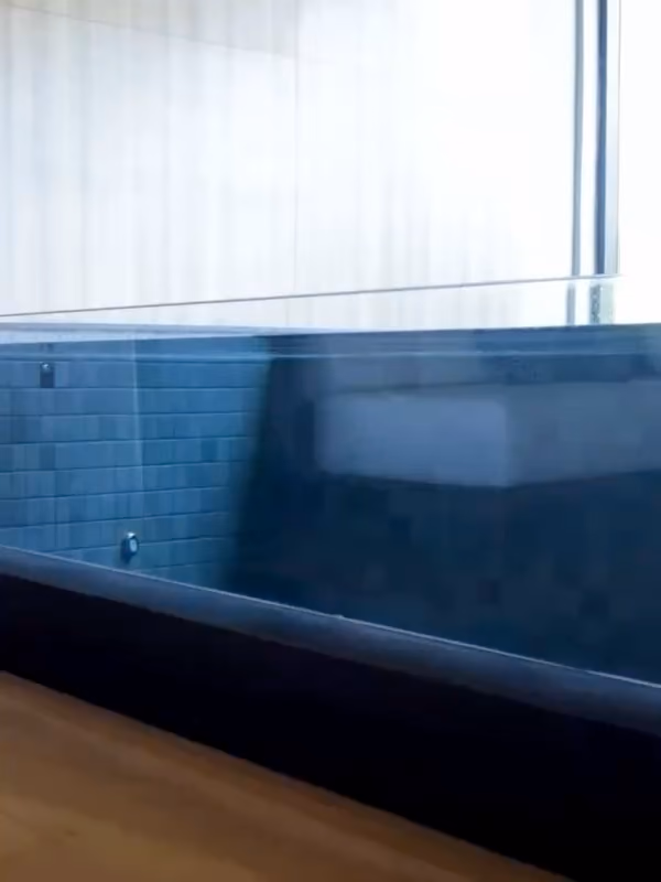 Bassin intérieur au carrelage sombre, paroi transparente, rideau clair derrière.