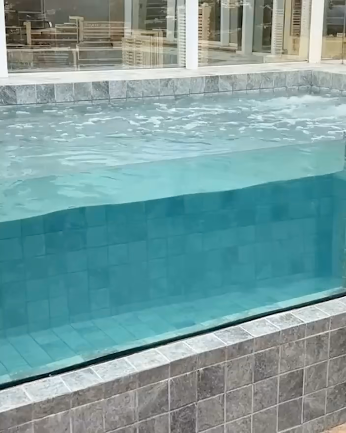 Gros plan sur une paroi transparente : l'eau turquoise et le carrelage se voient à travers.