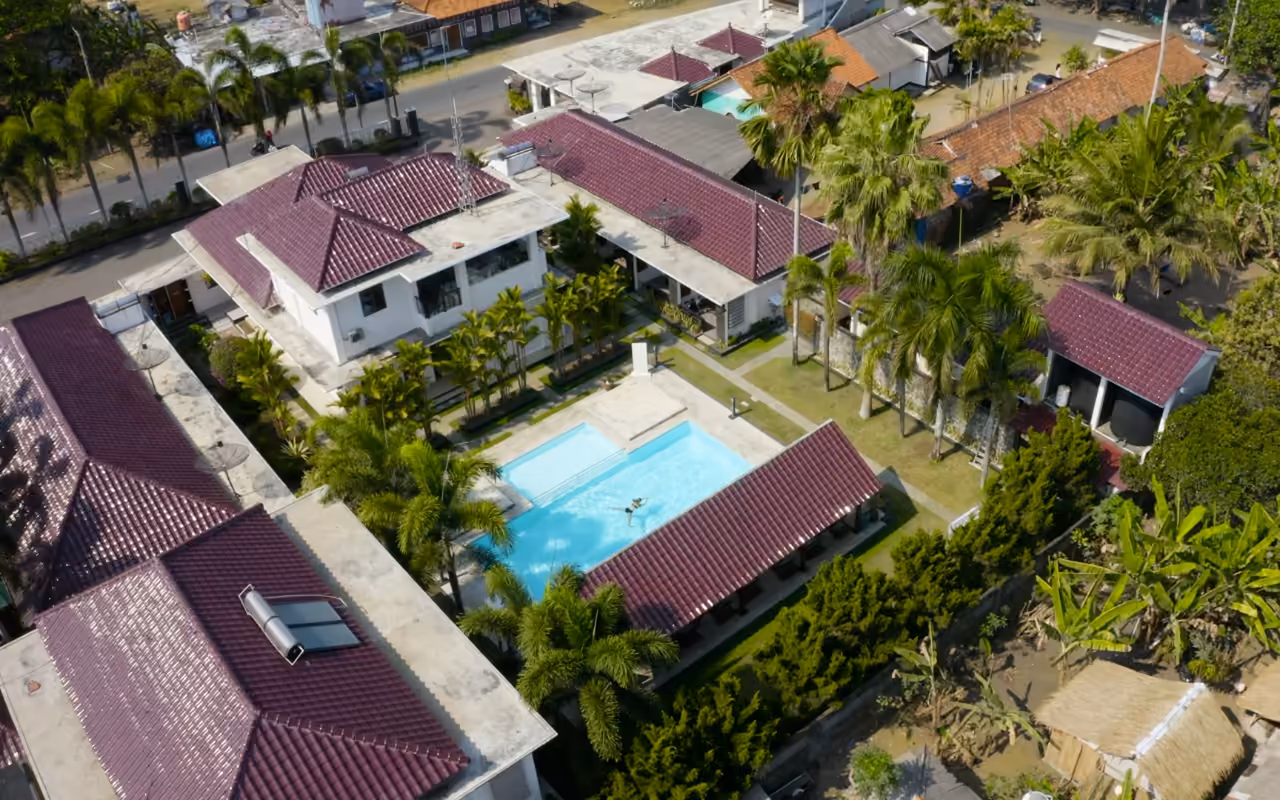 Vue du ciel : une villa à étage et sa piscine rectangulaire dans un jardin clos, au milieu d'un quartier arboré.