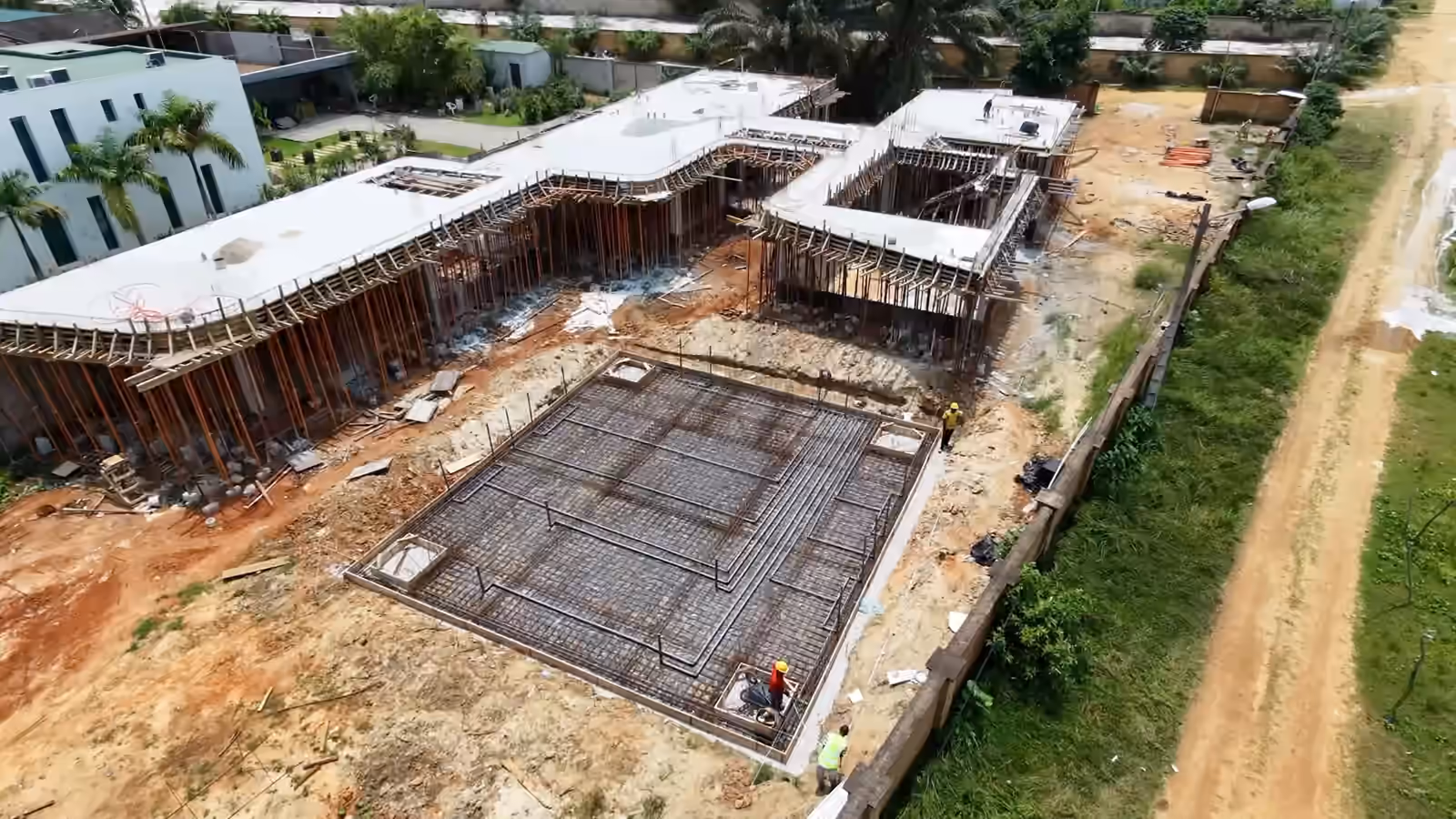 Vue de drone du chantier Villa Park : le radier ferraillé au premier plan, la structure en béton sous ses étais derrière, puis le même chantier vu en tournant autour.
