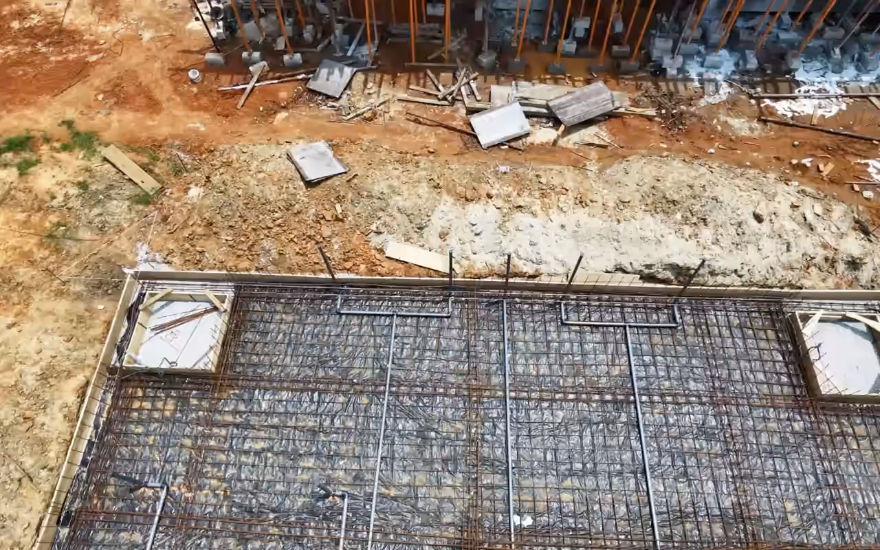 Vue de drone du chantier Villa Park : le radier ferraillé, puis la structure en béton et ses étais, vus de haut.