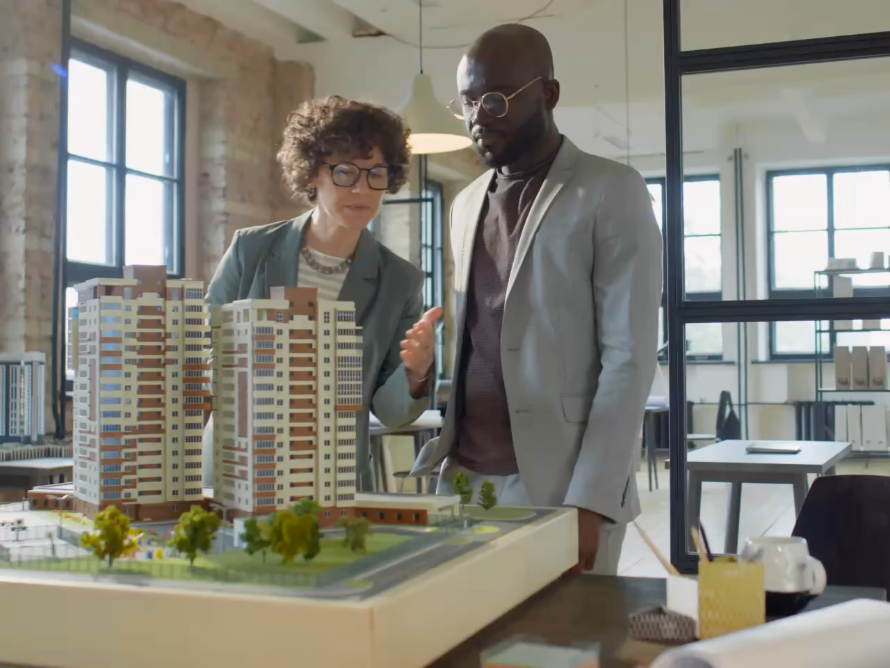 Deux personnes étudient la maquette d'un ensemble résidentiel : immeubles, jardins et allées.